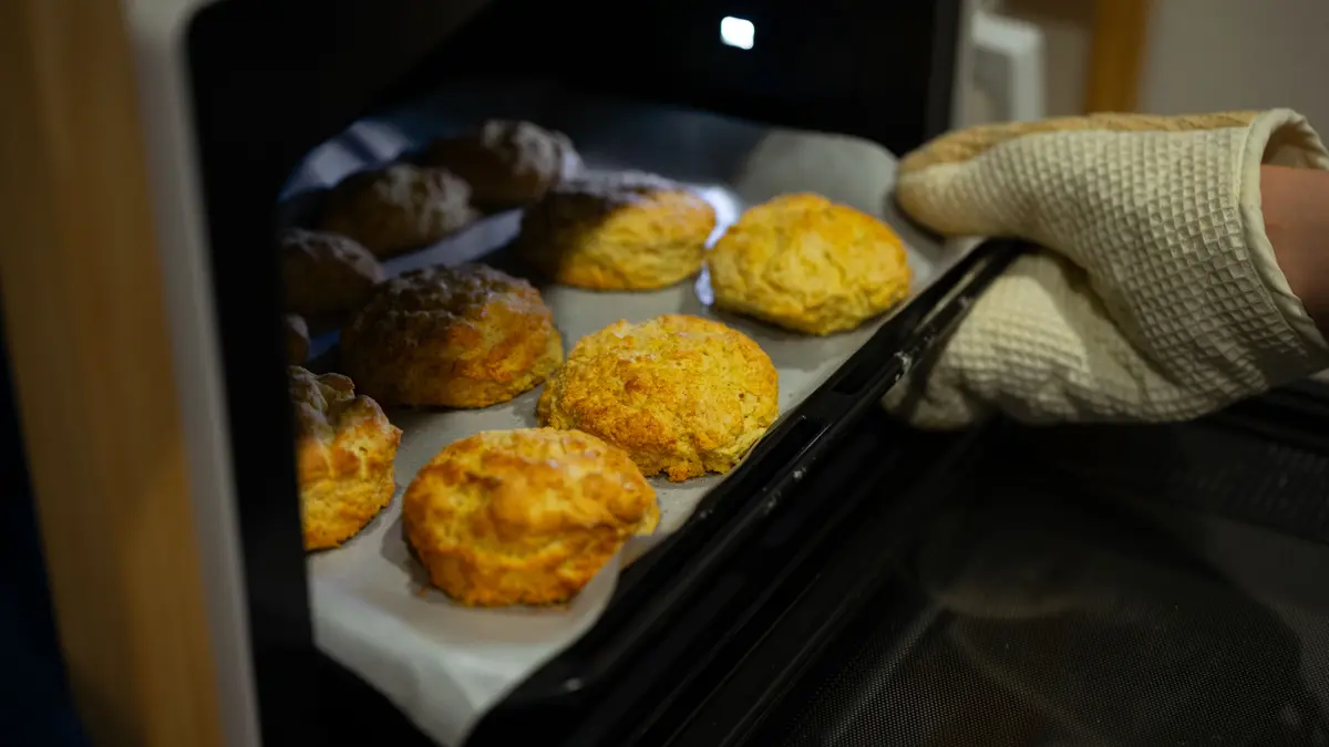 Hand met ovenwant die een bakplaat uit de oven haalt