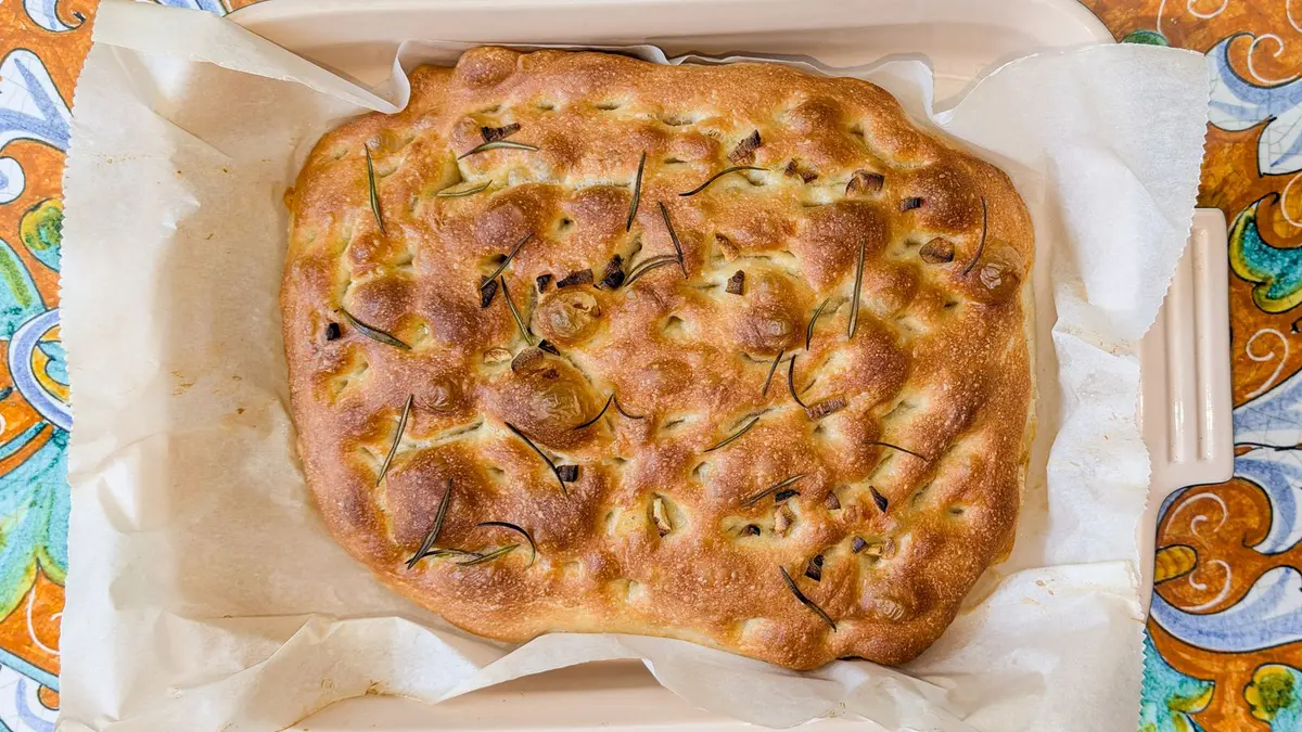 Goudbruine focaccia met rozemarijn en ui in een bakvorm, van boven gefotografeerd